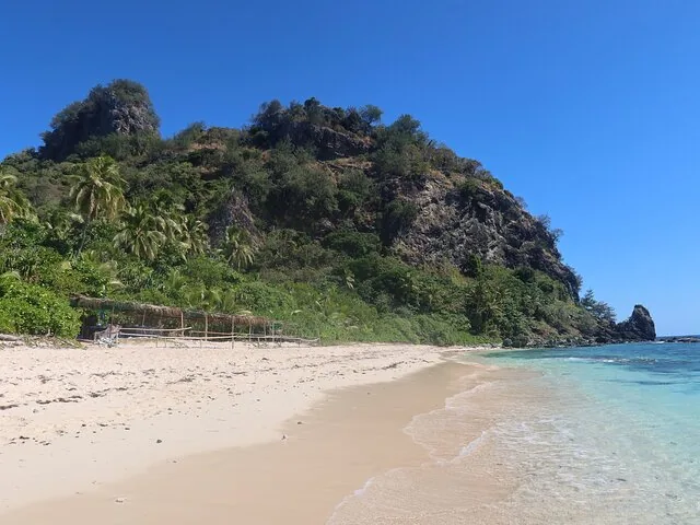 Sandstrand, der zu einem felsigen, baumbedeckten Hügel auf Monuriki führt.