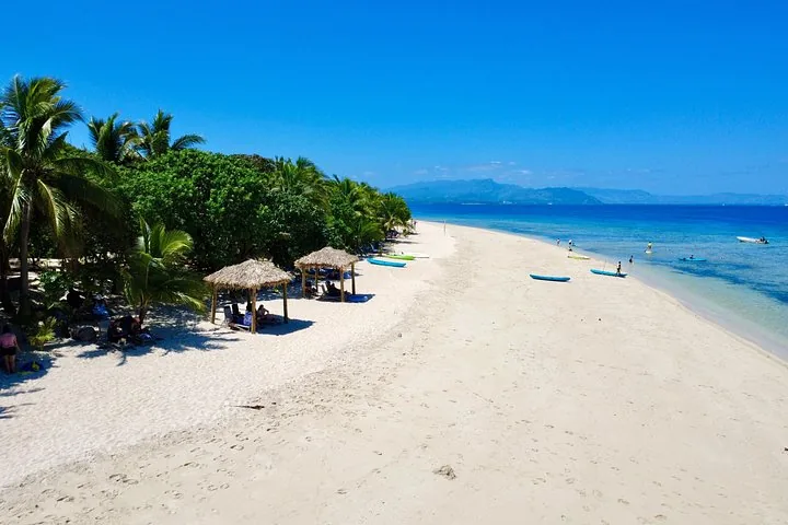 A long stretch of white sand beach with thatched umbrellas and kayaks.