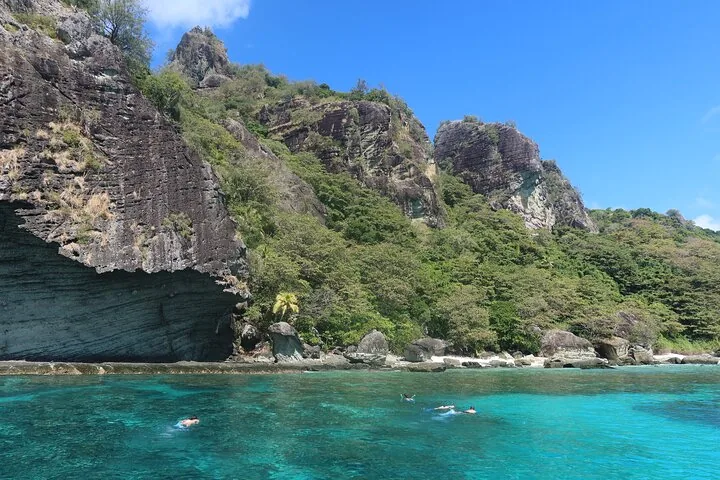 Menschen beim Schnorcheln in klarem blauem Wasser nahe steiler Felsklippen.