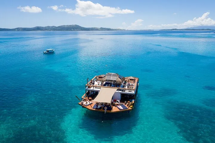 Eine mehrstöckige schwimmende Bar auf klarem türkisfarbenem Wasser, auf der Menschen entspannen.
